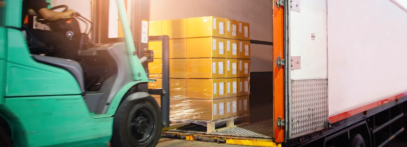 Forklift unloading a pallet of boxes off of a truck trailer into a warehouse