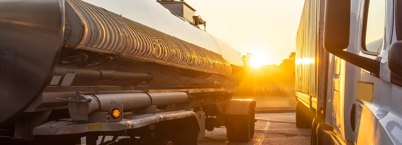 Liquid tanker trailer being pulled by a semi truck parked in a parking lot at sunset